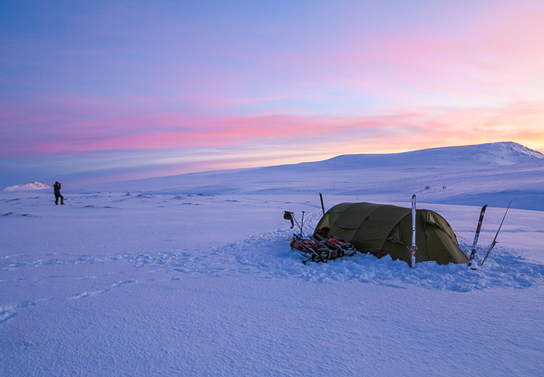 A tent pitched on the snow beneath a pink and blue sunset sky