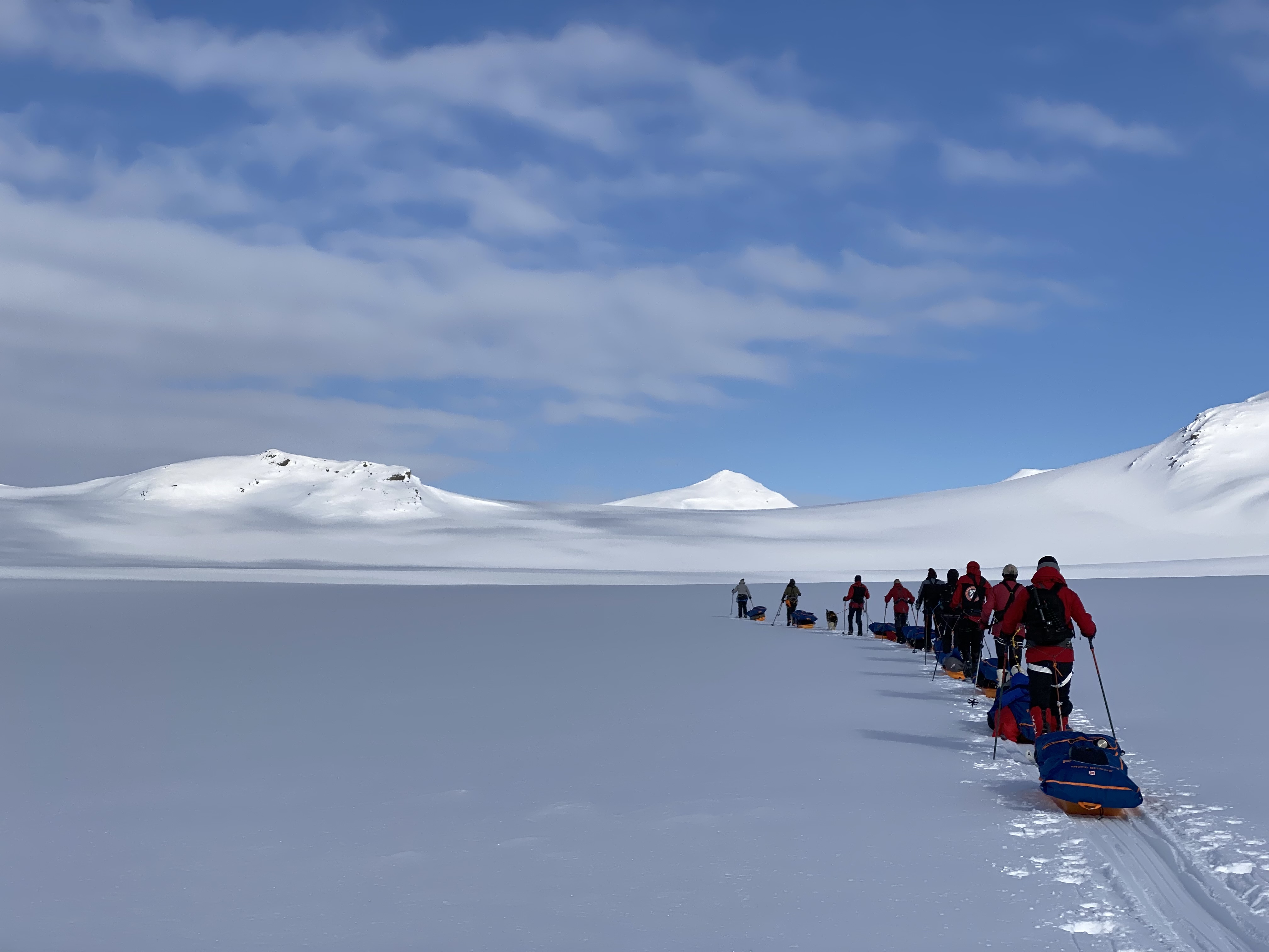 A line of skiers pulling sleds across a snow-covered plateau