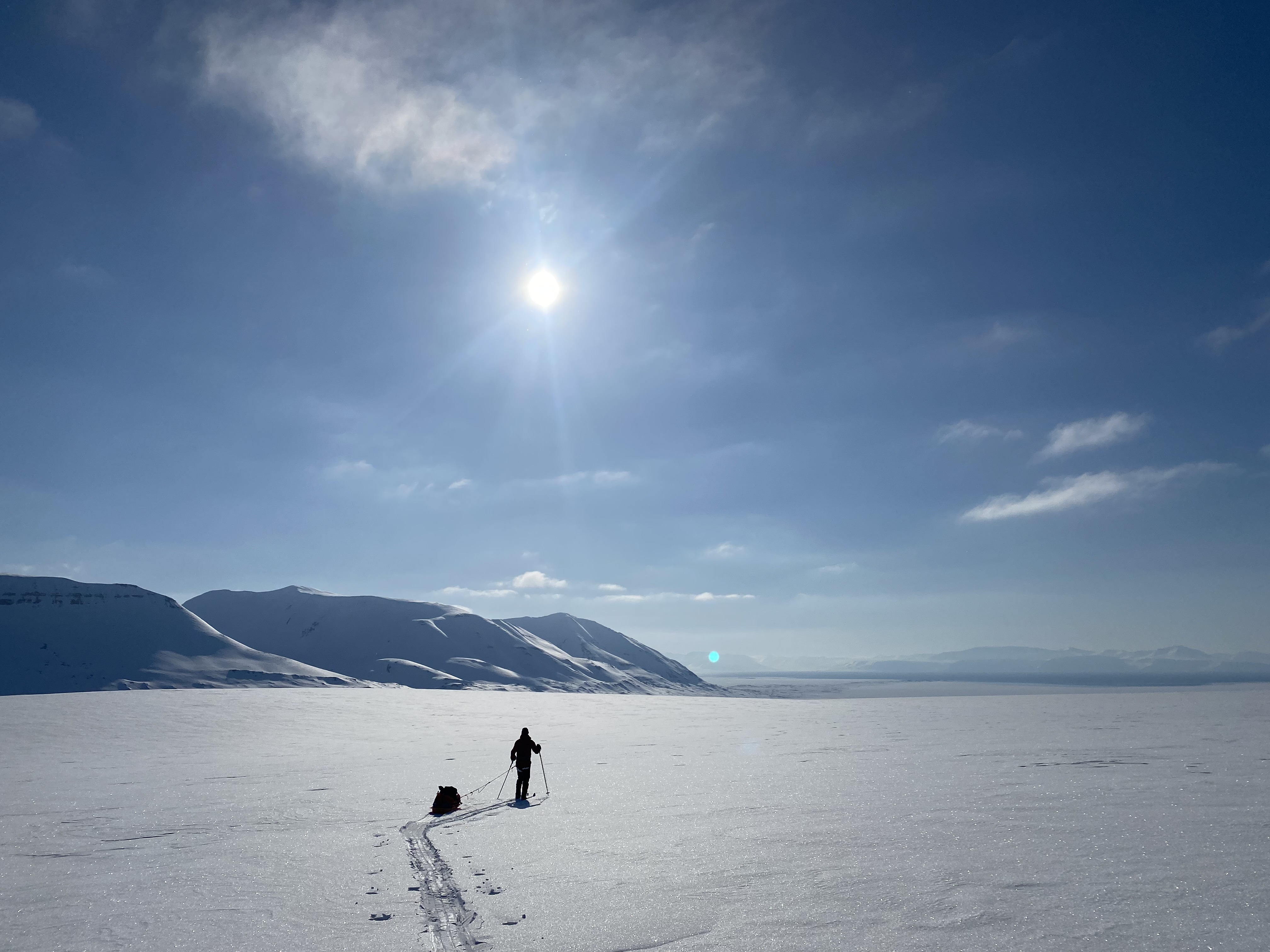 A lone skier pulling a sled across a glacier on Svalbard under a low arctic sun